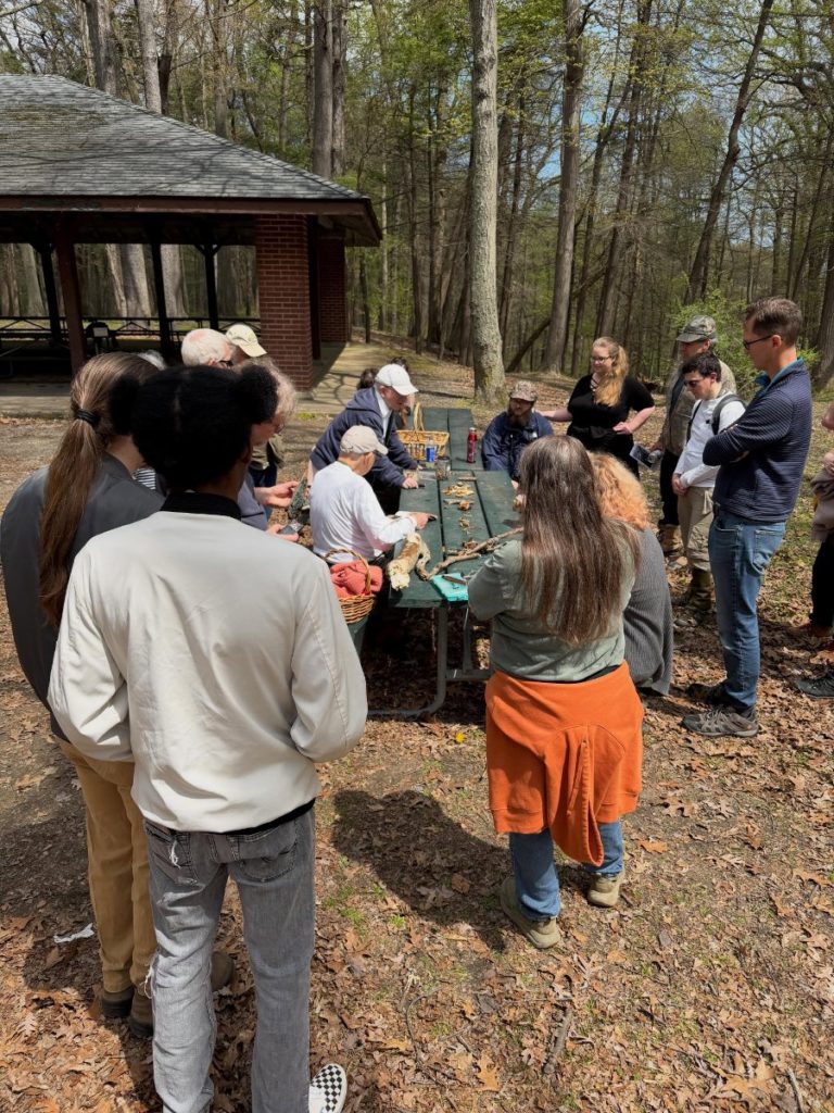 RAMA participants gathered around a picnic table examining finds beside a pavilion in the woods.